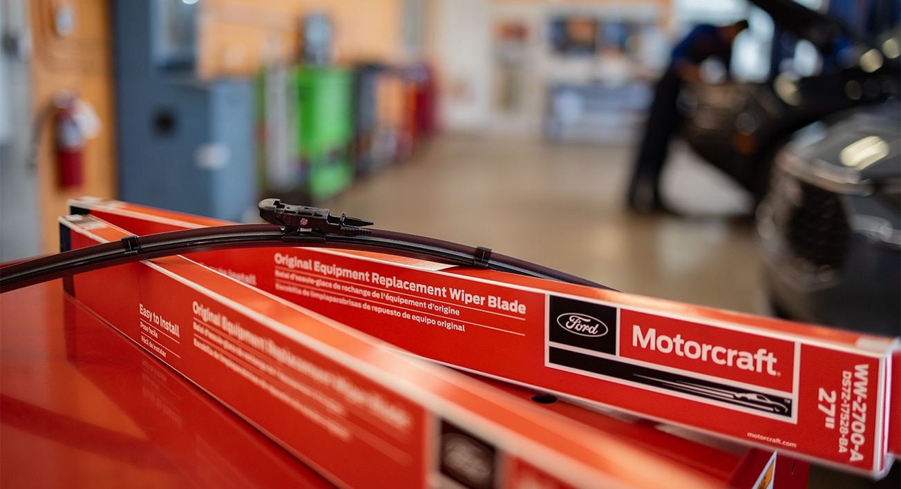 Un balai d’essuie-glace posé sur deux boîtes étiquetées « balais d’essuie-glace Motorcraft », sur un coffre à outils, dans un atelier de réparation.