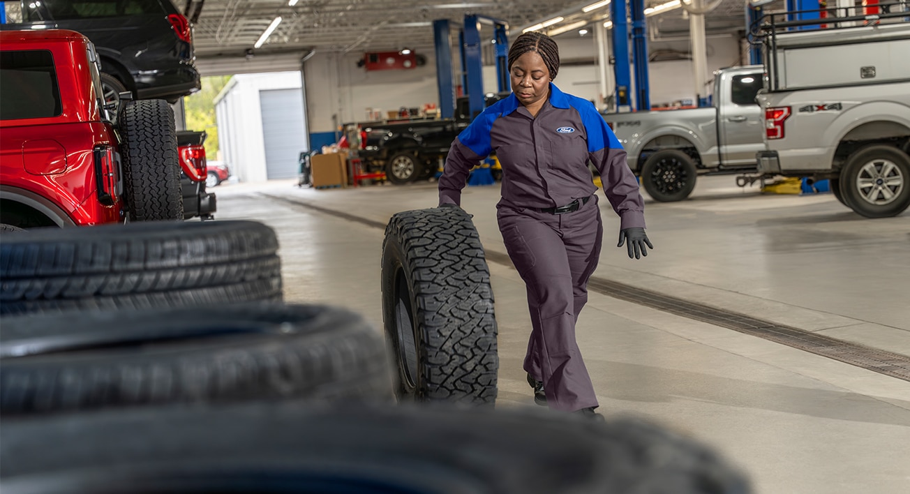 A Ford Service employee rolls a vehicle tire along the floor in a service centre.