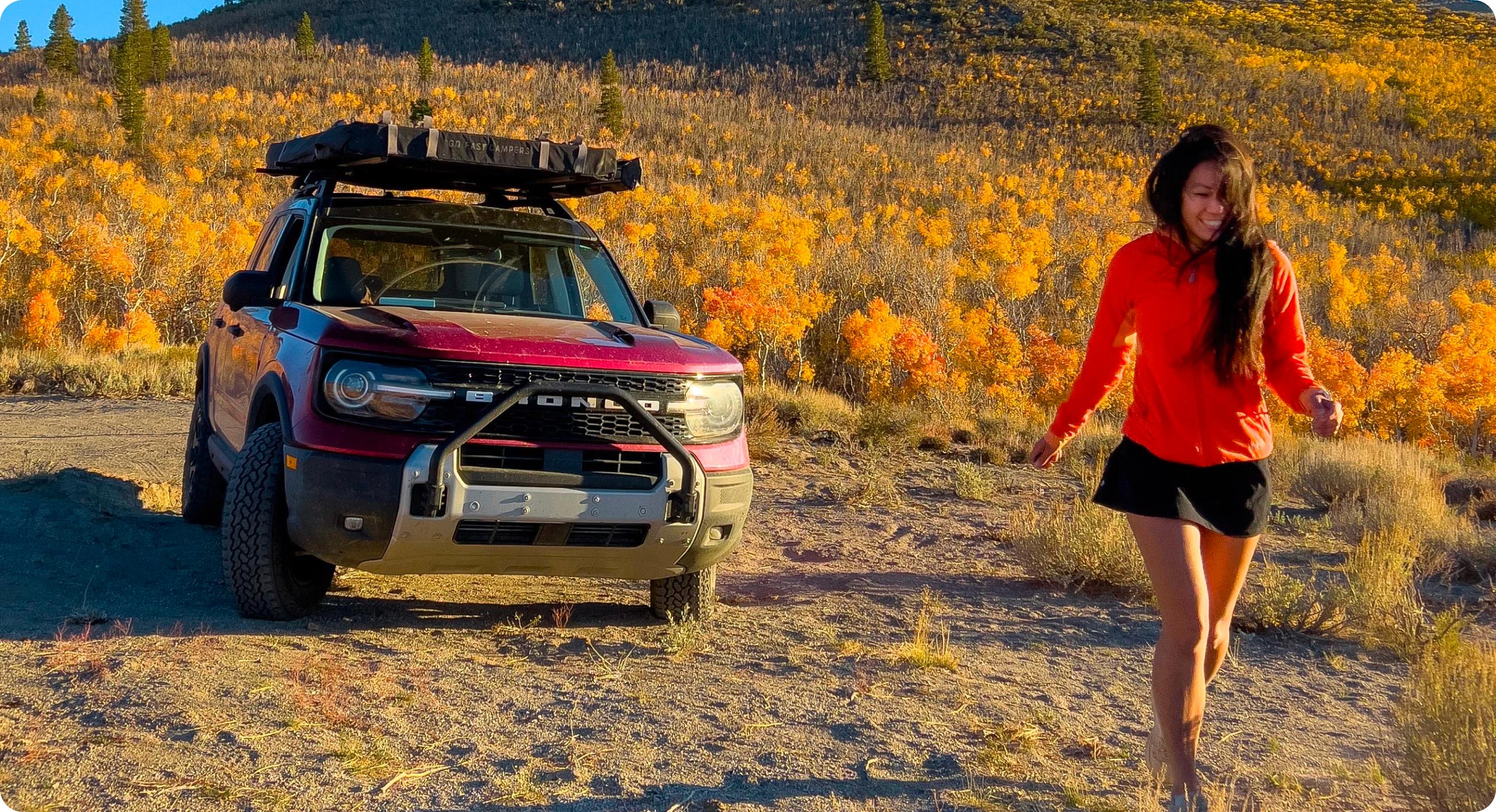 Une femme marche devant un Ford Bronco au coucher du soleil.