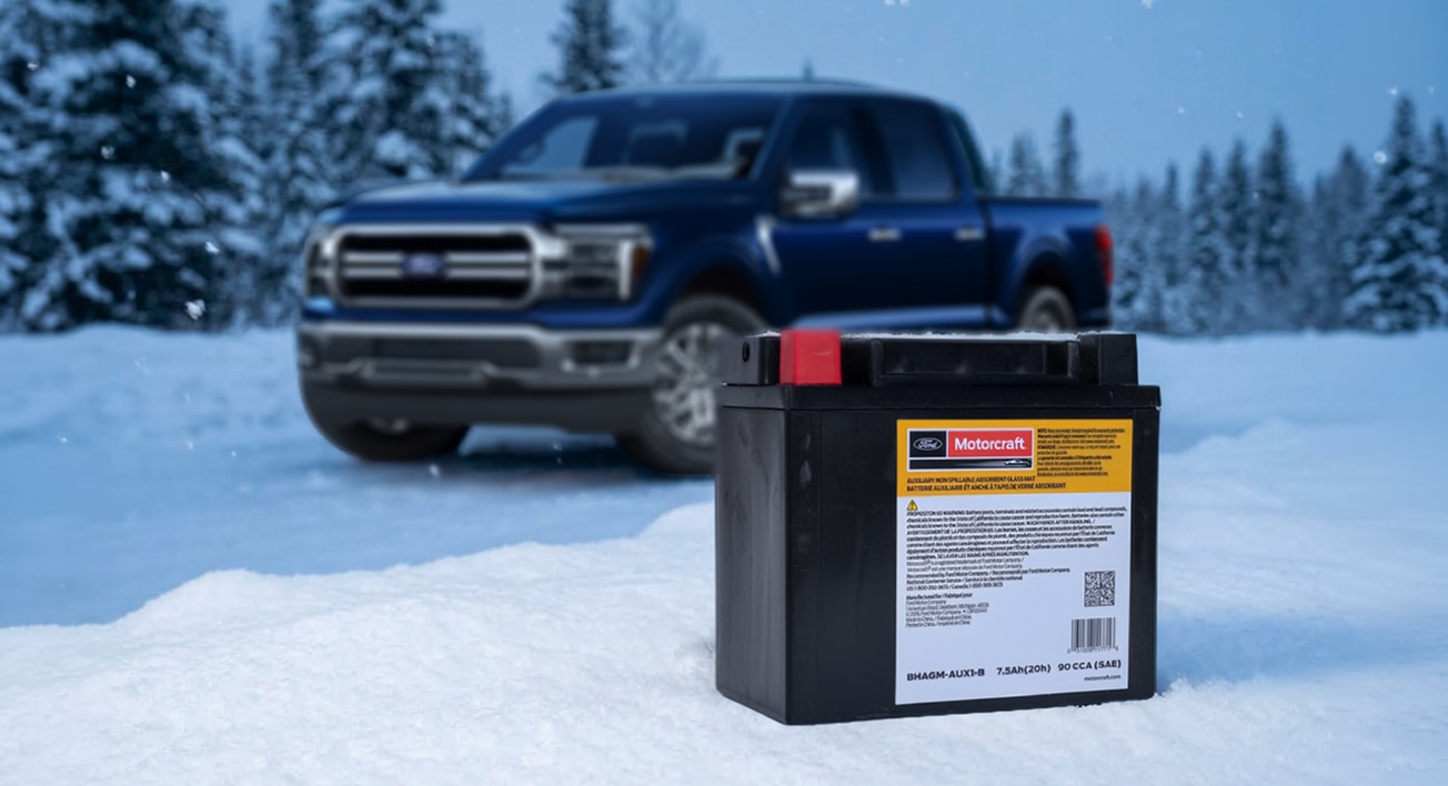 Une batterie Motorcraft posée dans la neige avec un Ford F-150 en arrière-plan parmi les conifères