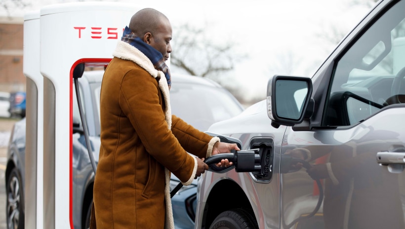 A man in a brown coat is charging his electric vehicle at a public charging station