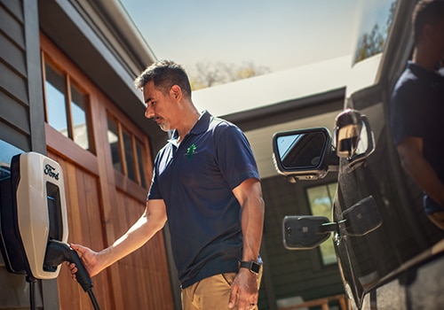 A man reaches for a Ford Connected Charge Station to plug into his Ford electric vehicle. 
