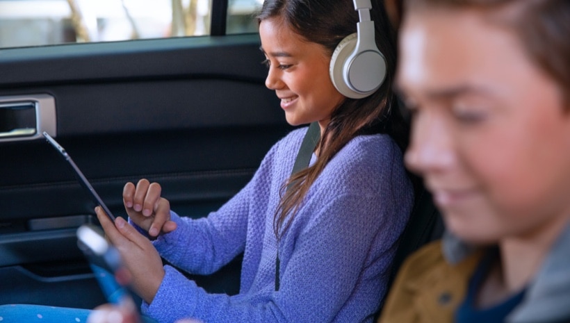 A boy and a girl in the backseat of a car using the available Ford wifi hotspot.