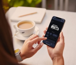 A woman holding a smartphone and viewing the Lincoln app in front of a cup of coffee.