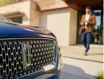 A man holding a smartphone viewing the Lincoln app walks toward the front grille of a Lincoln vehicle.
