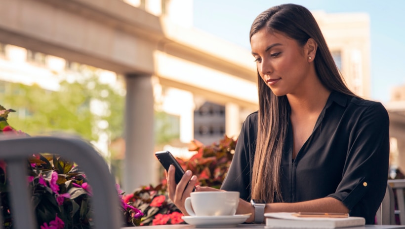 A woman sitting at an outside coffee table holding her smartphone and viewing the Lincoln app.
