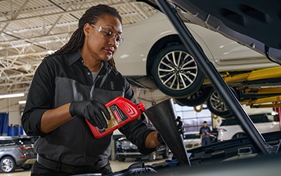 A Lincoln service tech adding oil to a vehicle.