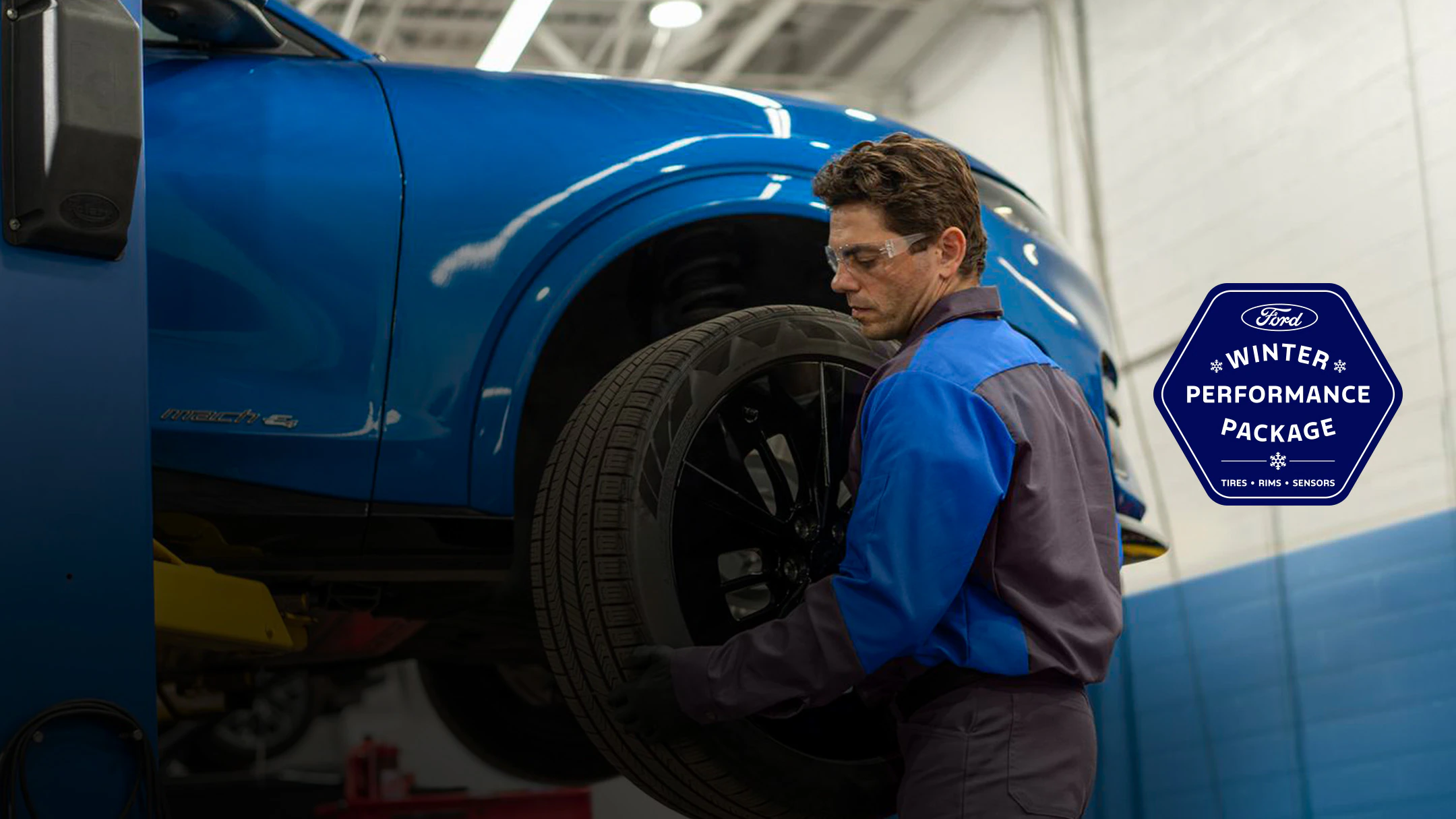 A Ford-trained technician installing a tire on a blue Mustang Mach-E. A logo for the Ford Winter Performance Package: Tires, Rims, Sensors, appears on the right