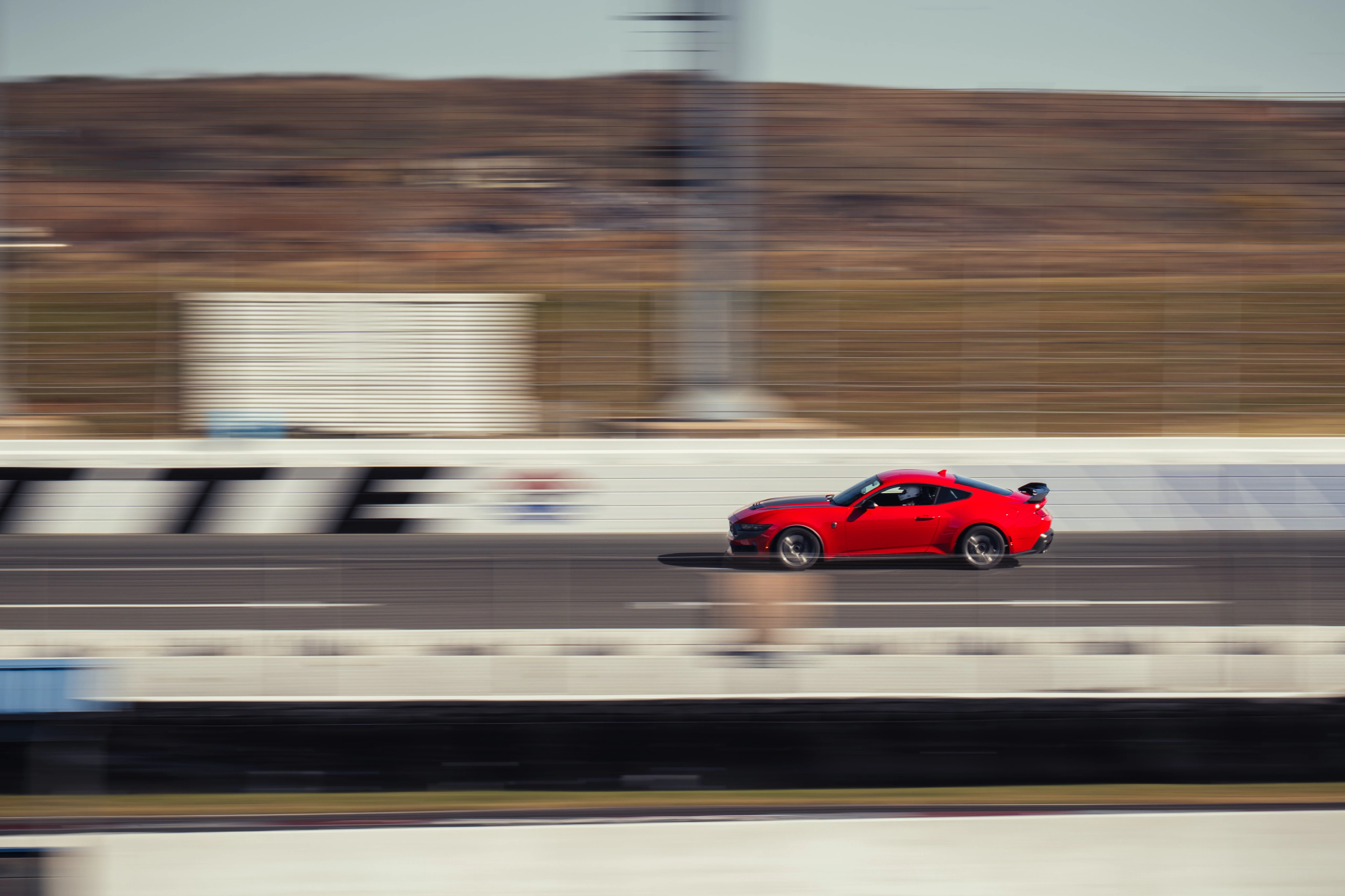 Red Ford Mustang sports car captured in motion on a roadway, showing dynamic speed with a blurred background