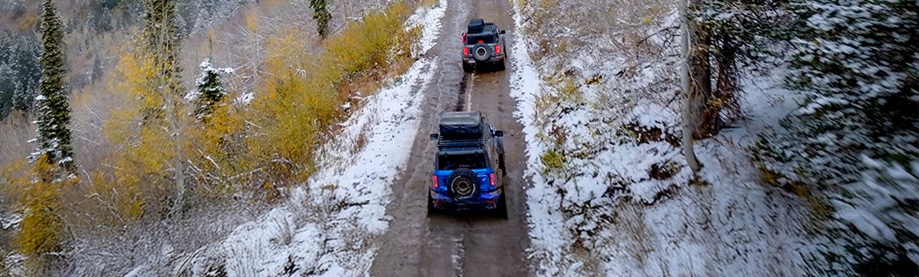 A couple of Bronco® SUVs navigate a trail that cuts through a snowy landscape.