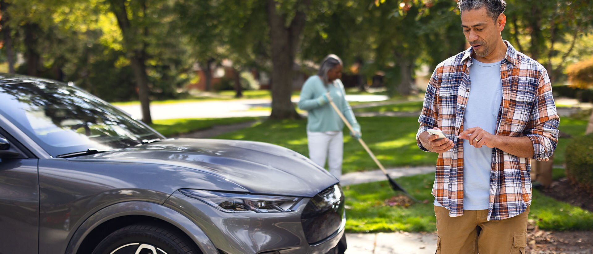 In a driveway standing next to a Ford Mach-E[REG] SUV, a Ford owner checks the Ford app on their phone