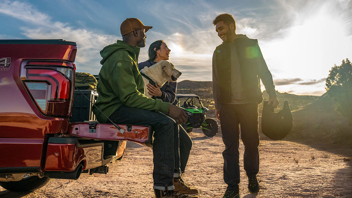 A group of friends and their dog gather around an open F 150 tailgate after riding 4 wheelers on a mountain.