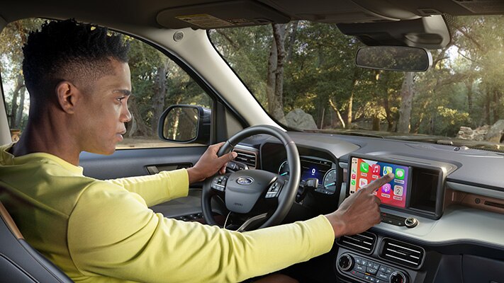 A driver in a parked 2023 Ford Maverick® truck with LARIAT® interior using the compatible Apple CarPlay® touchscreen menu.